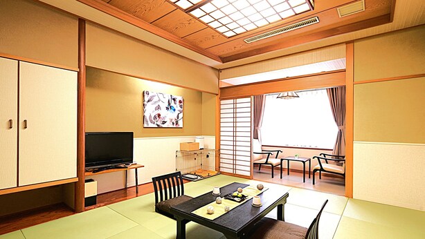 Una habitación tradicional japonesa con suelo de tatami, una mesa baja con cojines, un televisor y puertas correderas.