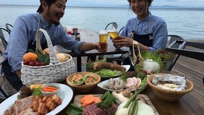 Two people sitting at a table with a variety of food items and drinks, overlooking a body of water. - Awaji TT House II Pacific Over Seas (Sumoto)