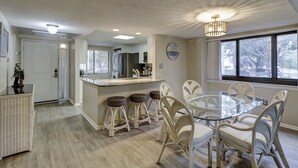 Uma cozinha moderna com uma ilha central, cadeiras de vime branco e uma mesa de jantar de vidro.