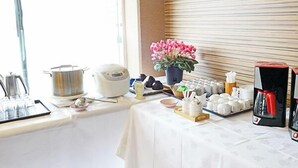Disposição para o café da manhã, com uma mesa, cafeteira, bule de chá e um vaso de flores.