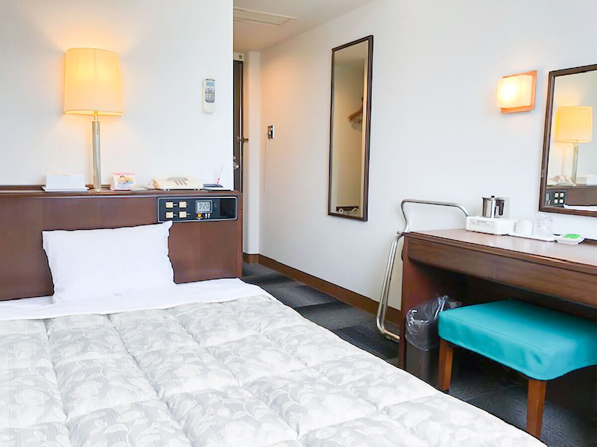 A hotel room with a bed, bedside table, lamp, desk, chair, and a mirror.