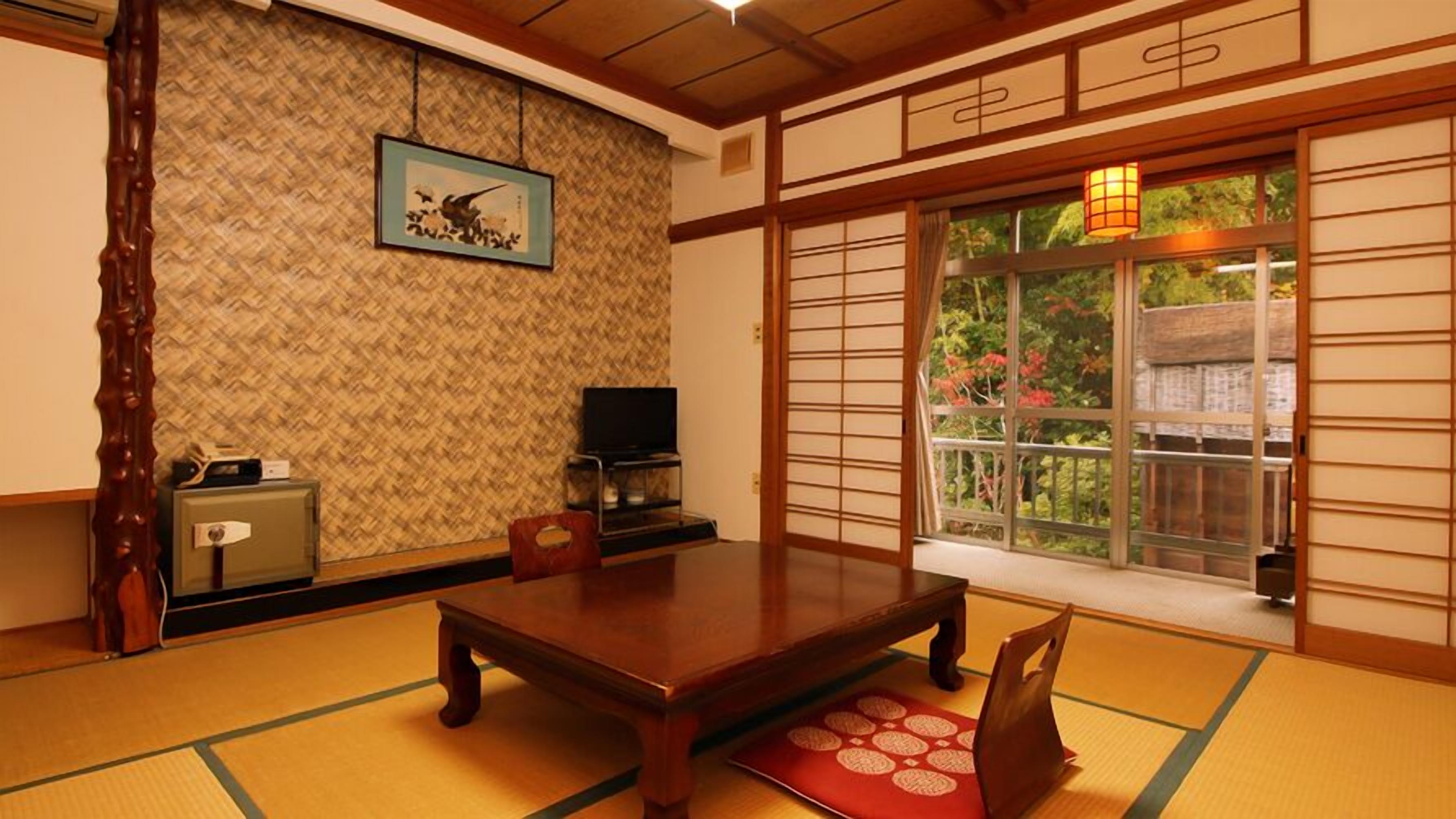 Une pièce de style japonais traditionnel, avec un sol recouvert de tatamis, une table basse, un téléviseur et une fenêtre donnant sur un paysage verdoyant.