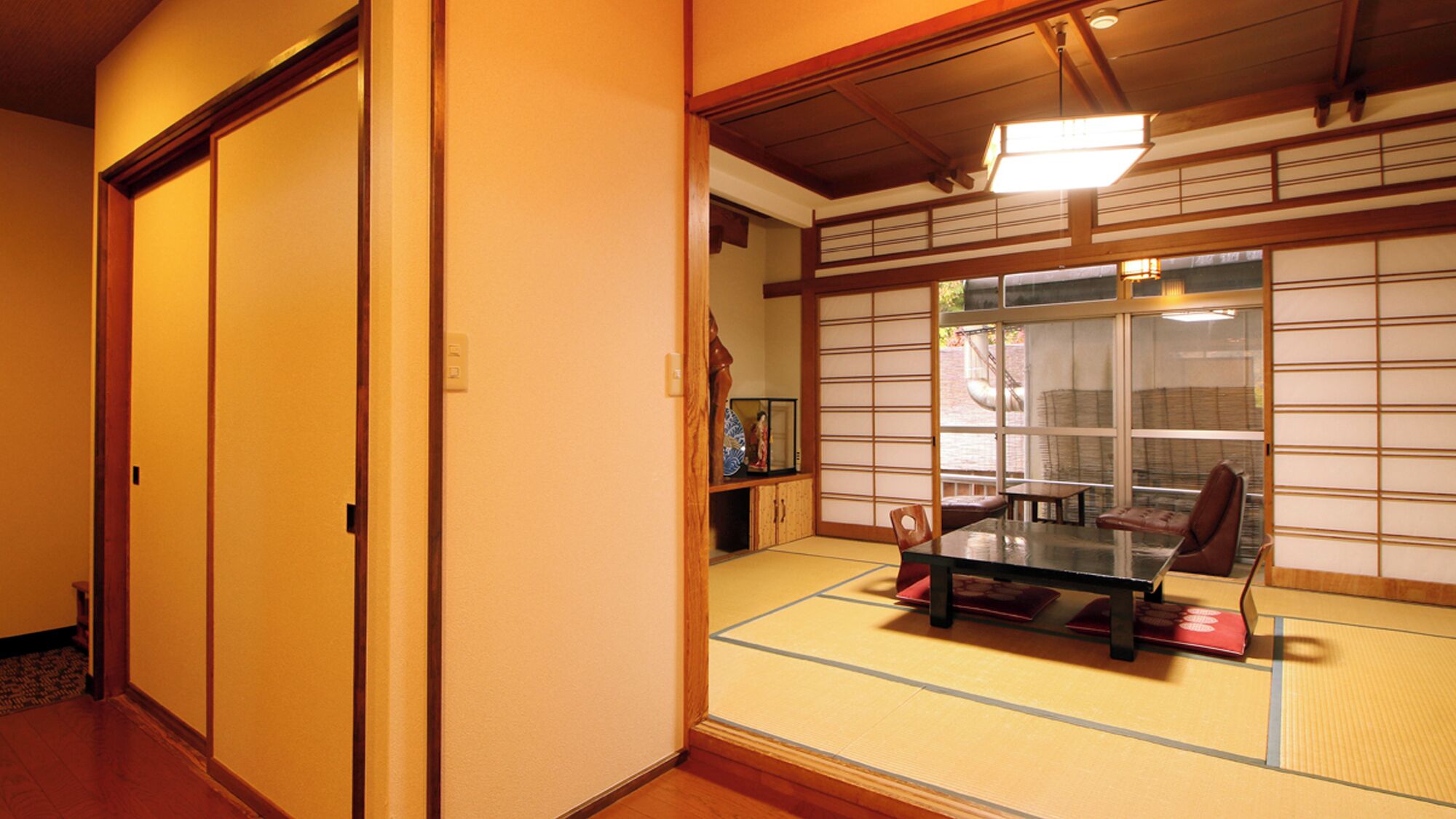 Una habitación japonesa tradicional con suelo de tatami, puertas correderas, una mesa con sillas y vistas a través de un celosía de papel.