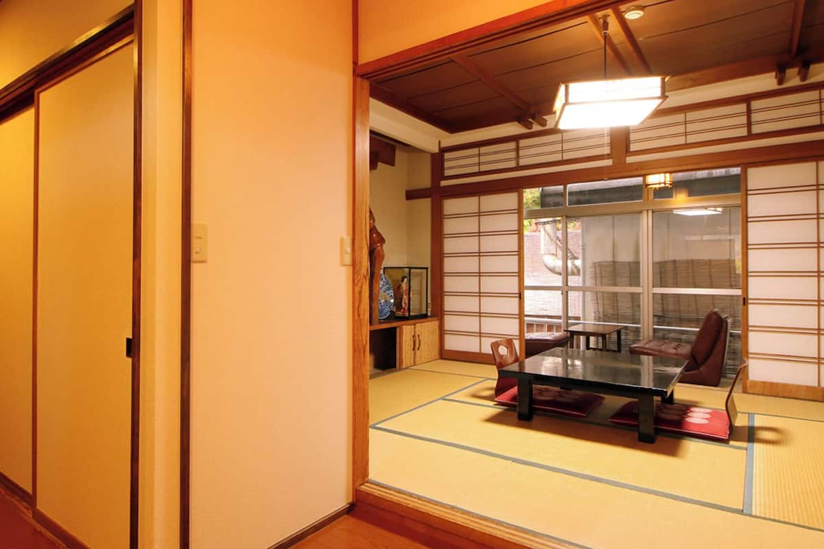 A traditional Japanese room with tatami flooring, sliding doors, a table with chairs, and a view through a shoji screen.