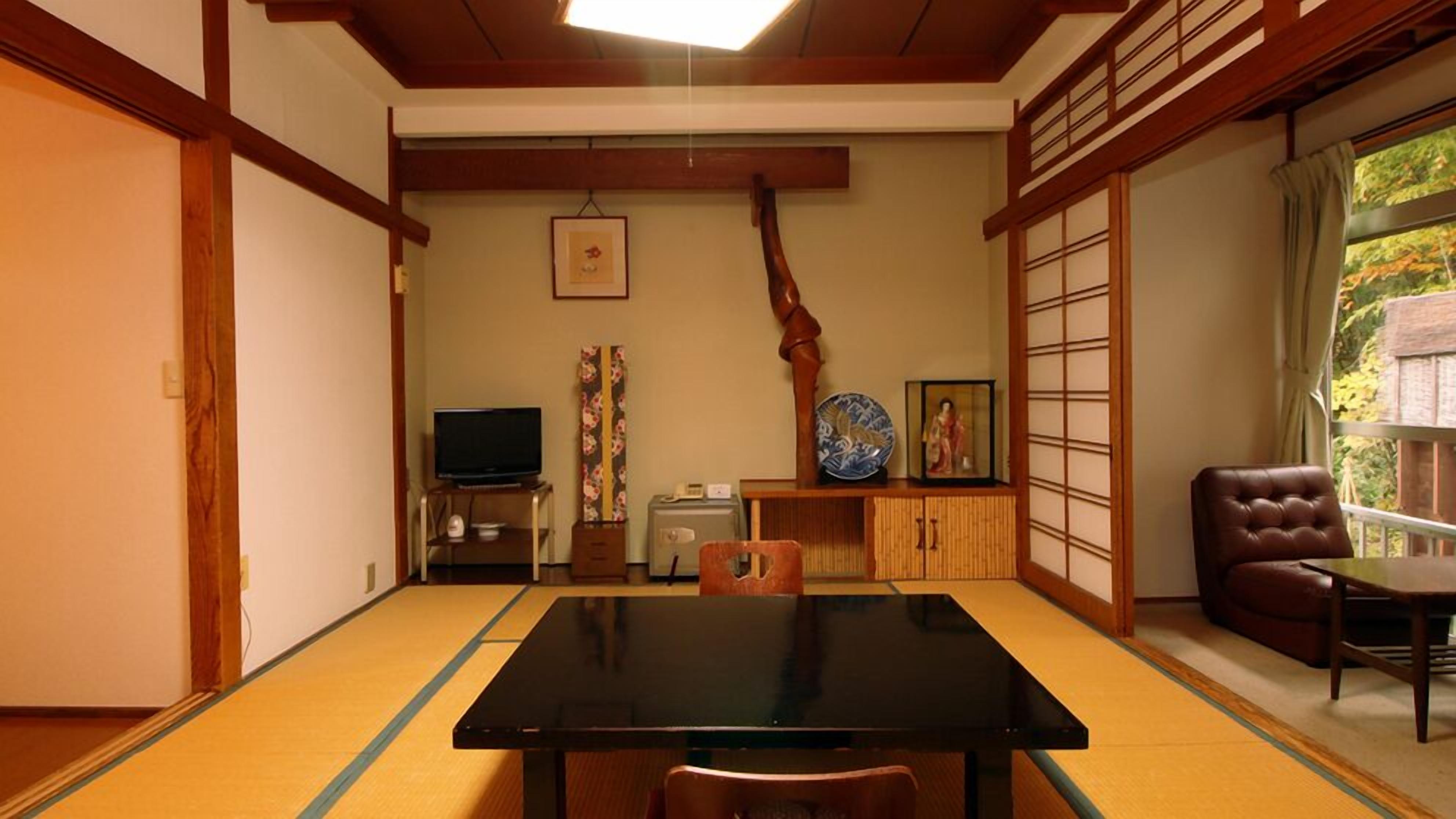 Une pièce de style japonais traditionnel, avec un sol recouvert de tatamis, une table noire, un téléviseur, un meuble contenant des objets décoratifs et une porte coulissante.