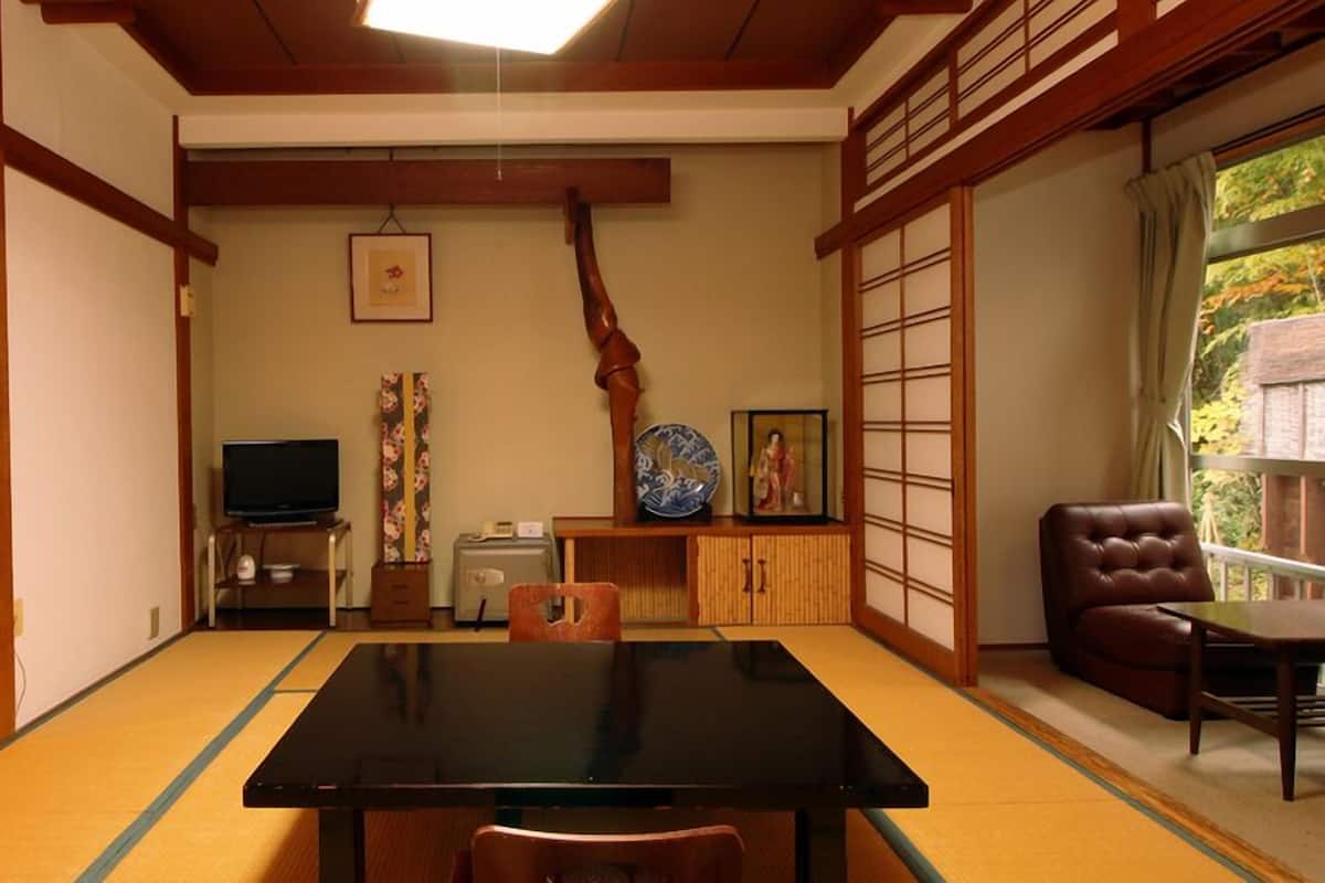 A traditional Japanese room with tatami flooring, a black table, a television, a cabinet with decorative items, and a sliding door.