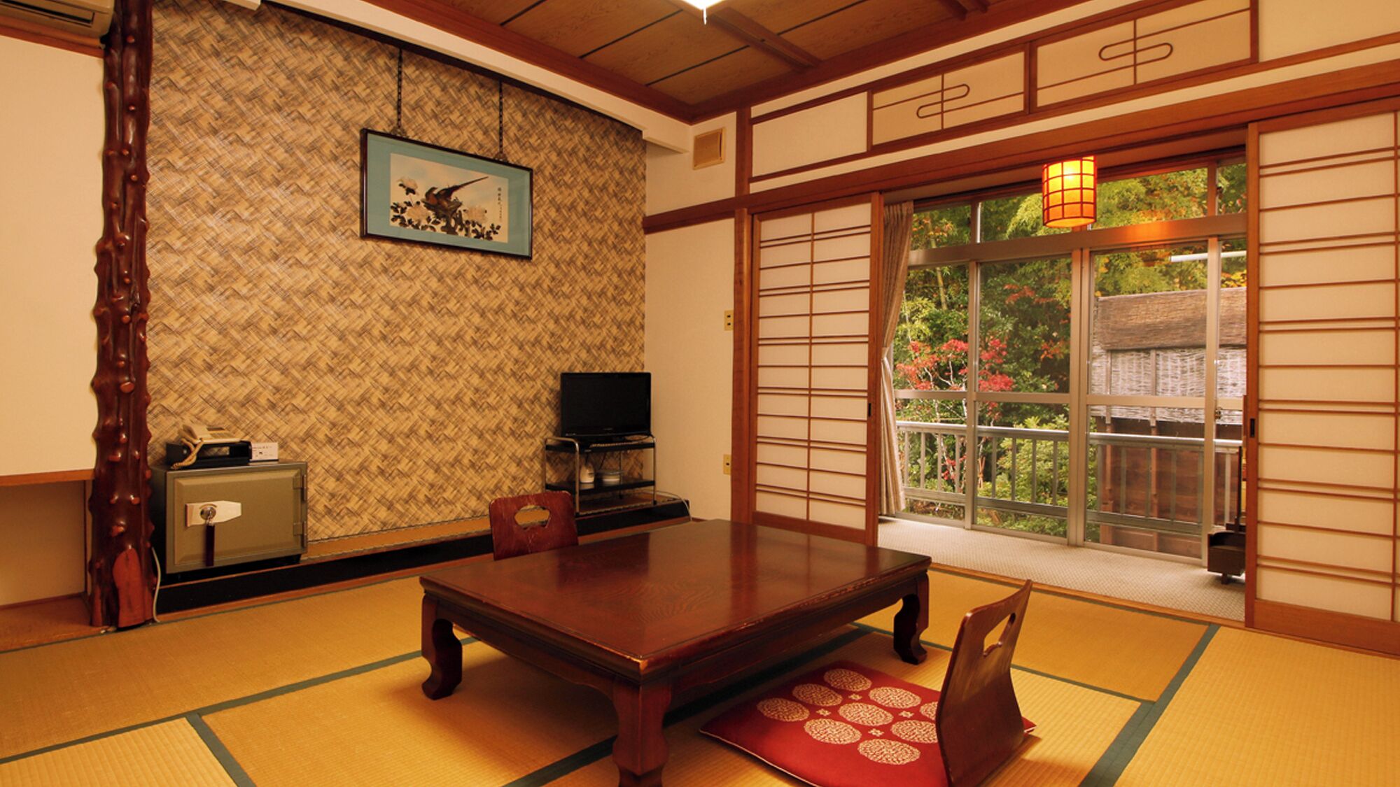 Una habitación japonesa tradicional con suelo de tatami, una mesa de madera, un televisor y una puerta corrediza con vistas a la vegetación.