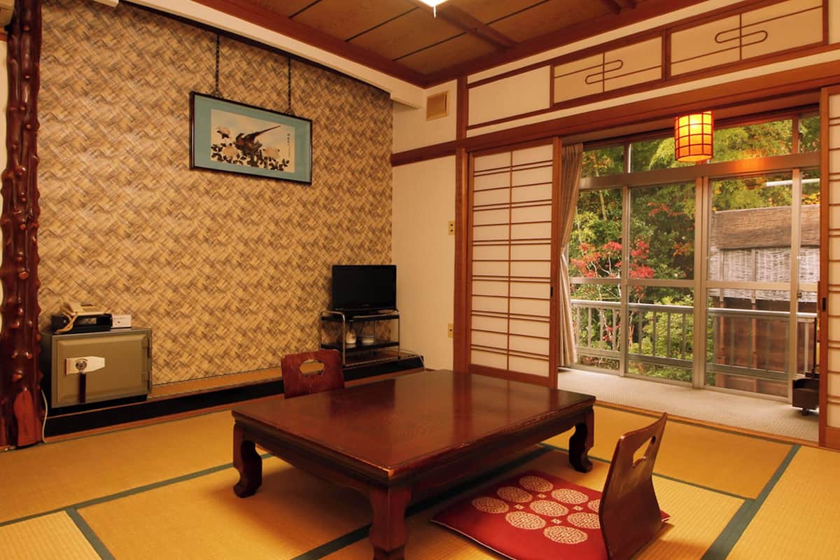 A traditional Japanese room with tatami flooring, a wooden table, a television, and a sliding door with a view of greenery.