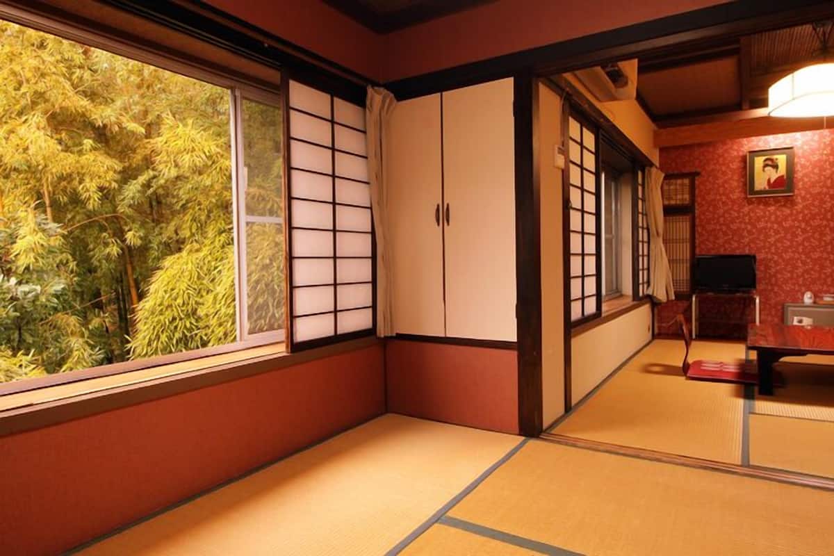 A traditional Japanese room with tatami flooring, sliding doors, and a view of trees.