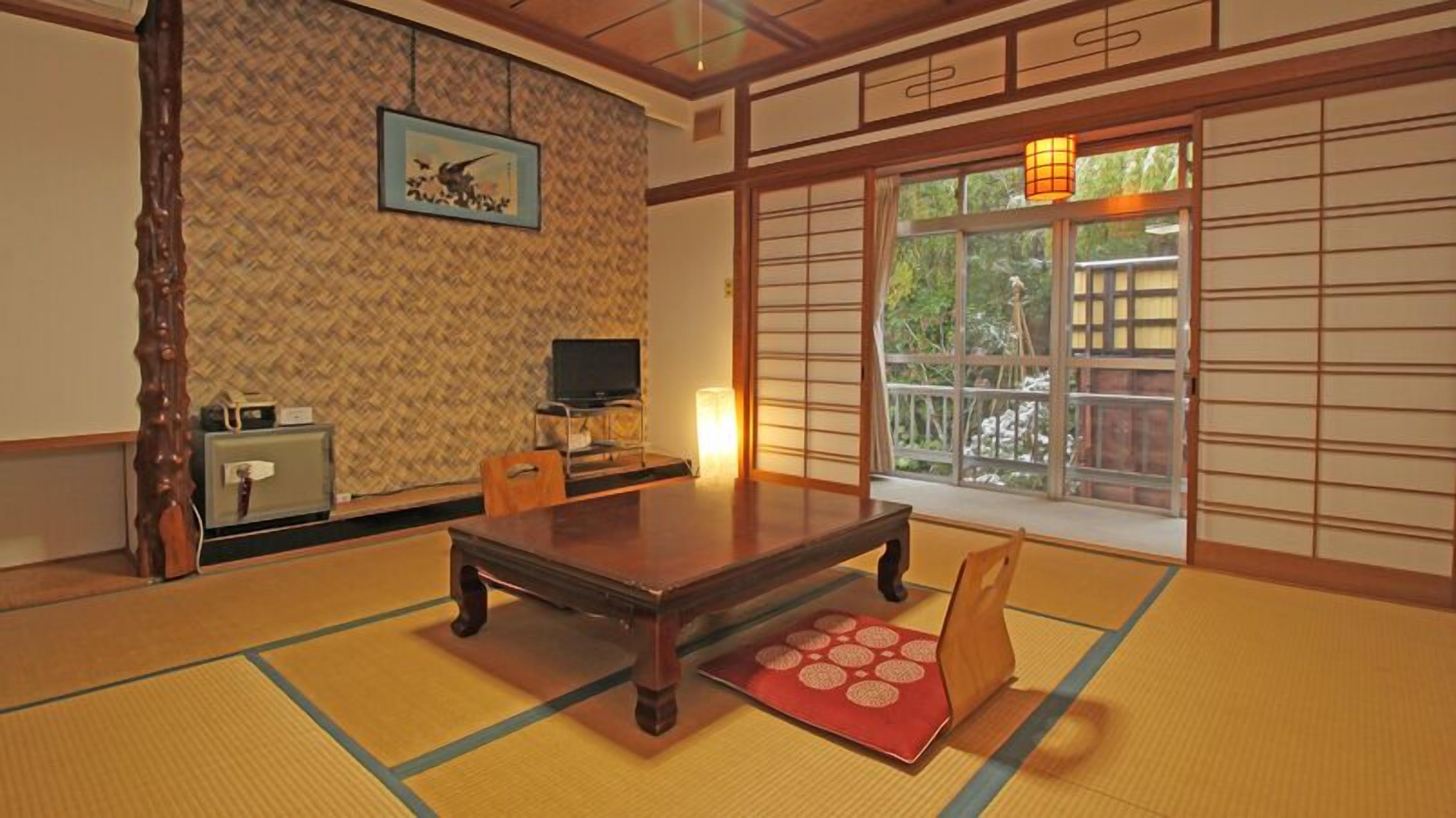 Une pièce de style japonais traditionnel, avec un sol recouvert de tatamis, une table basse, un téléviseur et une porte coulissante donnant sur un paysage.