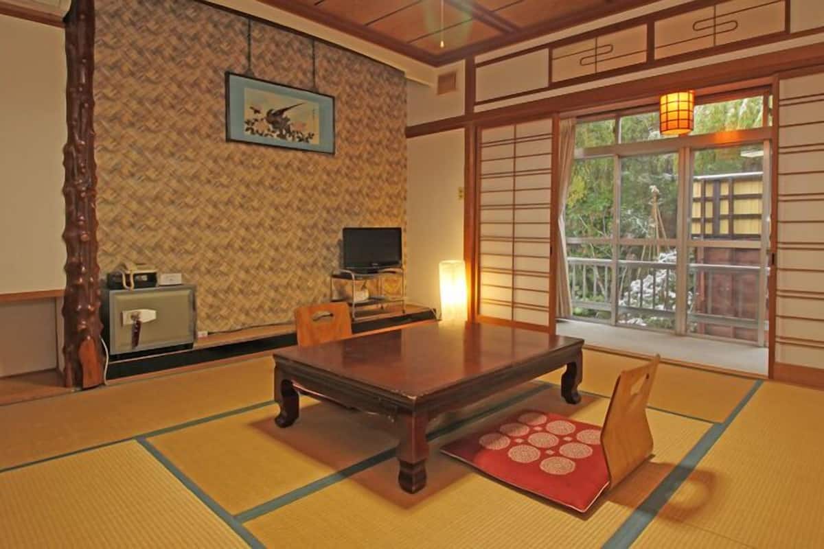 A traditional Japanese room with tatami flooring, a low table, a television, and a sliding door with a view.