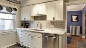 A modern kitchen with white cabinets, a stainless steel dishwasher, and a window providing natural light. - Fulton Retreat - Downtown Minneapolis - 50th and France! (Minneapolis)