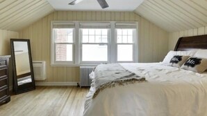 A bedroom with a sloped ceiling, a bed with white bedding, two windows, a radiator, and a dresser. - Fulton Retreat - Downtown Minneapolis - 50th and France! (Minneapolis)
