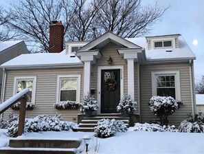 Stunning home with a central entrance, snow-covered landscaping, and a charming wreath above the door.