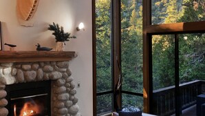 Ein gemütliches Wohnzimmer mit Kamin aus Stein, einer großen Dekoration mit Hirschgeweih und Blick auf eine Berglandschaft durch große Fenster.