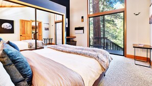 Ein Schlafzimmer mit einem großen Bett, einem Schreibtisch und Blick auf einen Wald durch ein großes Fenster.