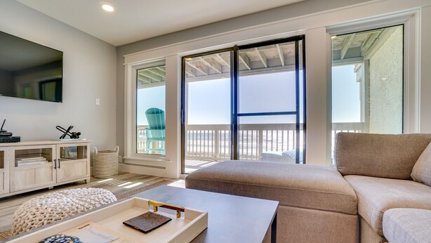 A living room with a beige sofa, a coffee table, a TV, and a balcony with a view of the beach. - Ramsgate 22 | Renovated Gulf-Front Escape (Panama City Beach)
