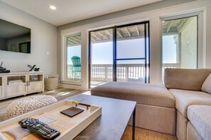 A living room with a beige sofa, a coffee table, a TV, and a balcony with a view of the beach. - Ramsgate Harbour 22 - Gulf Front • Huge Balcony • Beach Service (Panama City Beach)
