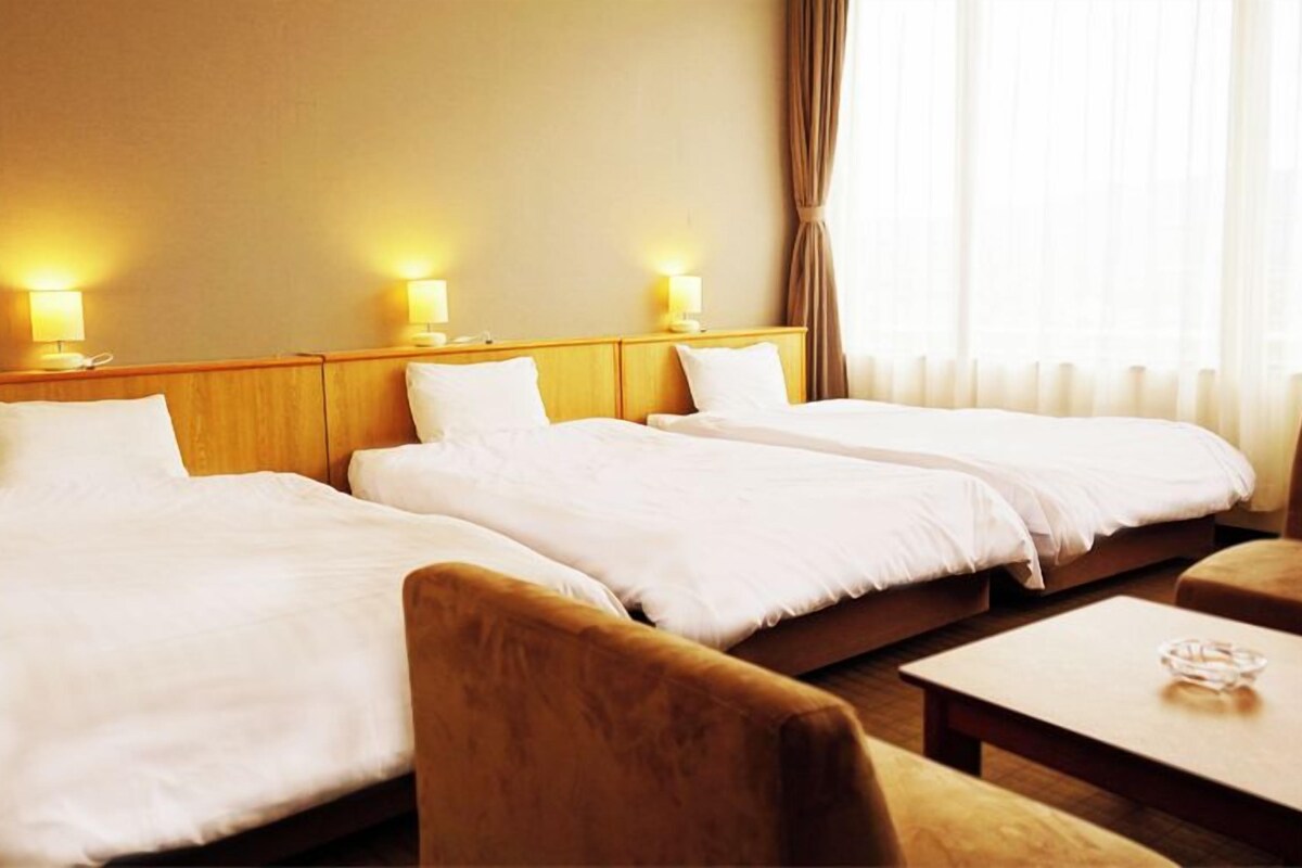 Ein Hotelzimmer mit zwei Einzelbetten, einem Holzkopfteil, Nachttischlampen, einem Holztisch und einem Stuhl.