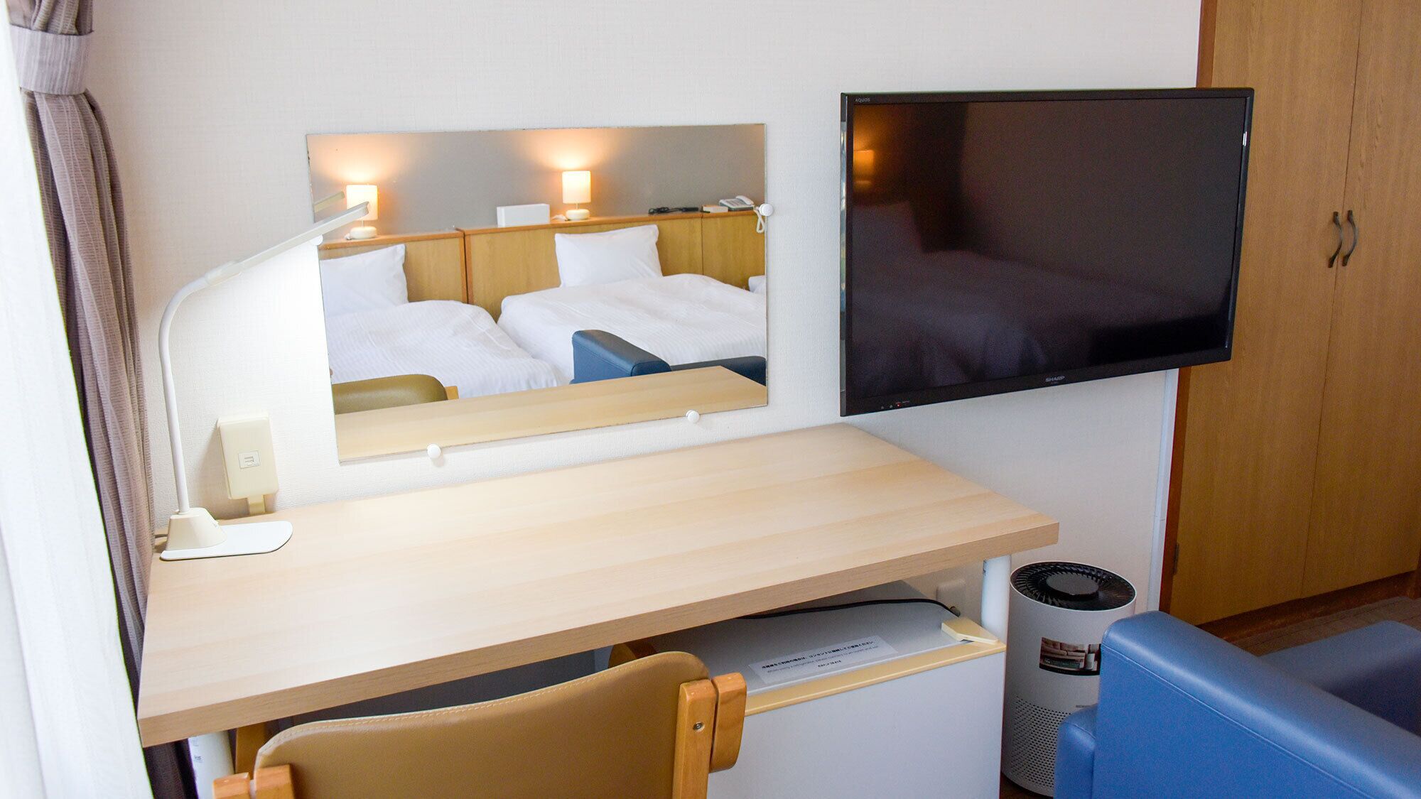 A hotel room with a bed, a desk with a chair, a television, and a mirror.