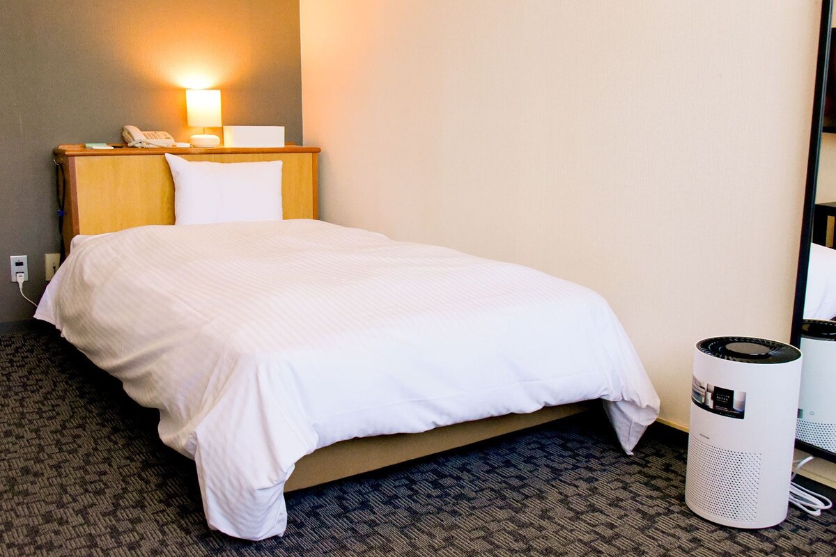 Ein Hotelzimmer mit einem Bett, einem Nachttisch mit Lampe, einem Telefon und zwei weißen Mülleimer.