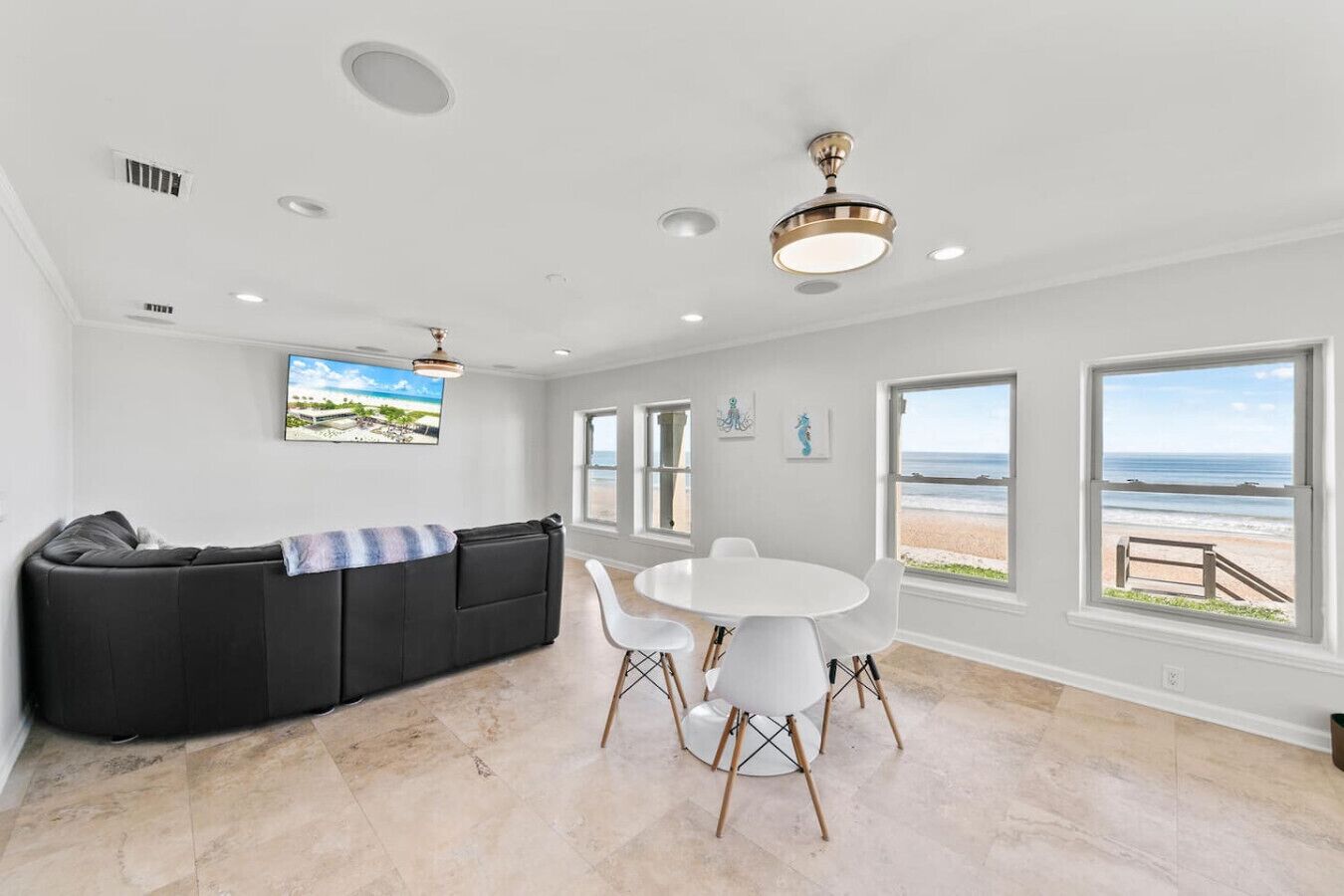 Ein modernes Wohnzimmer mit einer schwarzen Couch, einem runden weißen Tisch und großen Fenstern mit Blick auf den Strand.