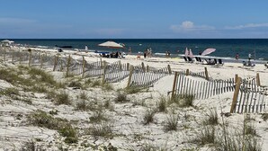 Ein Strand mit einer Holzbank, Liegestühlen, Sonnenschirmen und einigen Personen.