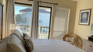 Ein Schlafzimmer mit einem großen Bett, einem Deckenventilator, Blick auf einen Balkon und einem Korbstuhl mit Kissen.