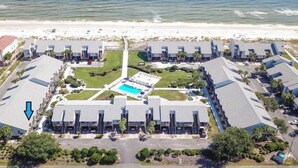 Eine Luftaufnahme eines Küstenhotels mit mehreren Gebäuden, einem zentralen Pool und einem Strand im Hintergrund.