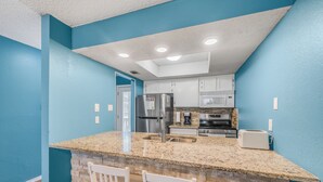 A kitchen with blue walls, a granite countertop, white cabinets, stainless steel appliances, and two white chairs.