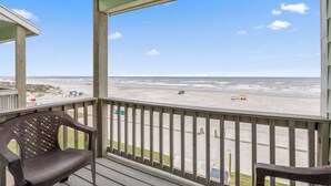 A wooden deck with two chairs, overlooking a beach with a sandy shore and ocean waves.