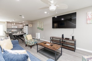 A modern living room with a sofa, coffee table, TV, and a dining area with chairs and a table.