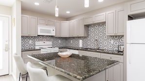 A modern kitchen with a central island, white cabinets, a patterned backsplash, and pendant lighting. - Beachfront Condo | Stunning Ocean & Pool Views, 3 Balconies (Corpus Christi)