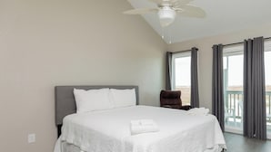 A bedroom with a large bed, a ceiling fan, a chair, and a view of the outdoors through a window. - Beachfront Condo | Stunning Ocean & Pool Views, 3 Balconies (Corpus Christi)