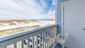 A balcony with a view of the beach, a white door, and parked cars. - Beachfront Condo | Stunning Ocean & Pool Views, 3 Balconies (Corpus Christi)
