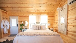 Ein Schlafzimmer einer Holzhütte mit einem Bett, zwei Nachttischen, einem Spiegel und einer Tür.