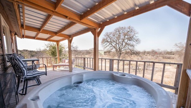 Ein Whirlpool mit Holzterrasse und Stühlen, umgeben von einer Holzbrüstung und Blick auf eine trockene Landschaft.