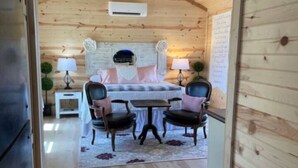 Ein gemütliches Holzhaus-Interieur mit Essbereich, inklusive Tisch und vier Stühlen, Deckenventilator und einem Bett mit Kopfteil.