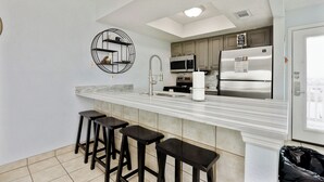 A modern kitchen with a marble countertop, stainless steel appliances, and a circular wall shelf. - Beachside Condo | Pet-Friendly, Balcony Views & Coastal Charm (Corpus Christi)