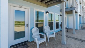 A building with a number 114 sign, two white Adirondack chairs, and a covered porch area. - Beachside Retreat | Pool, Hot Tub & Beach Access (Corpus Christi)