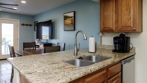 A kitchen with granite countertops, a stainless steel sink, wooden cabinets, a coffee maker, and a painting on the wall. - Pet-Friendly Coastal Retreat | Pool, Hot Tub & King Bed (Corpus Christi)