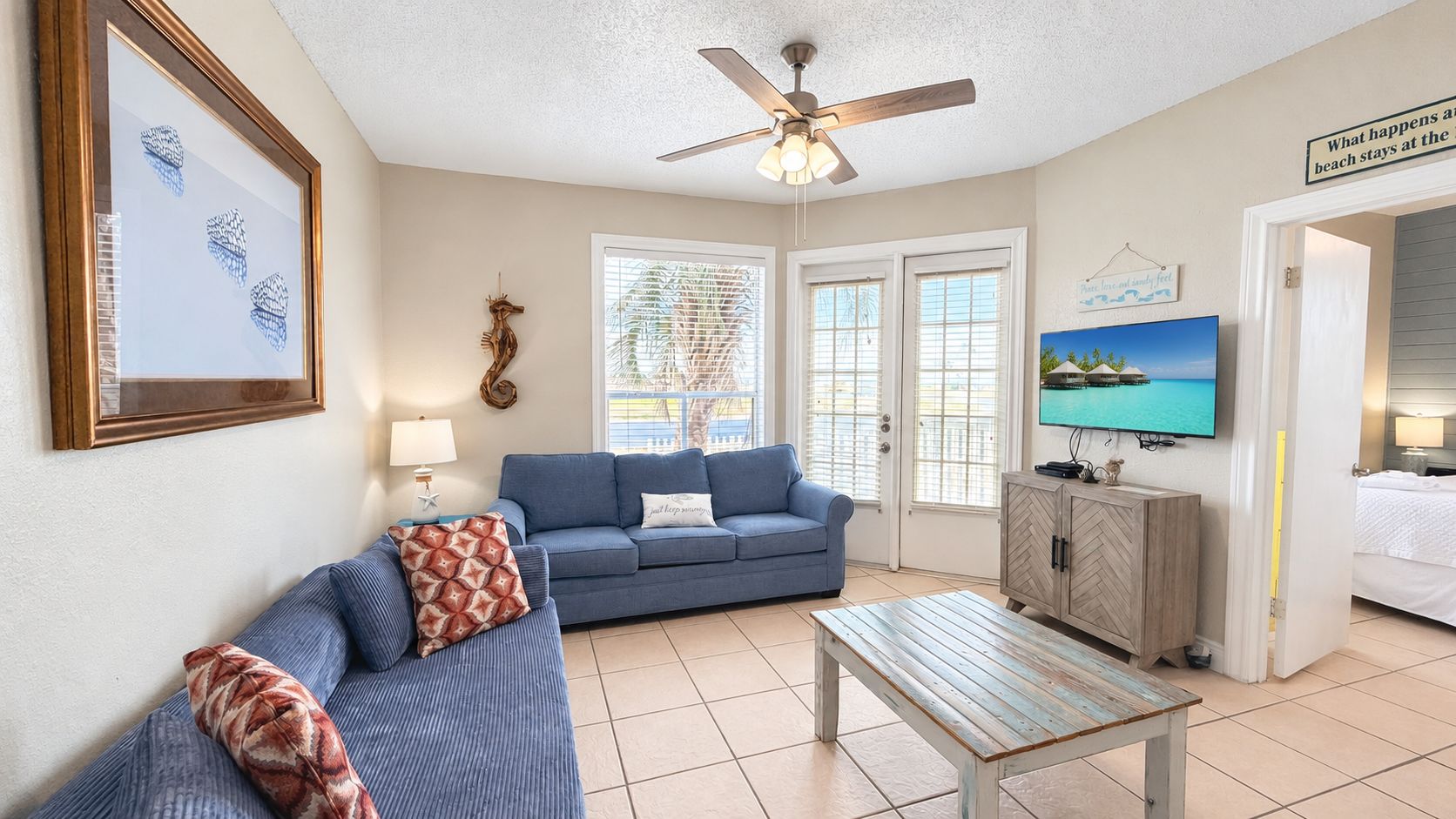A living room with a blue sofa, a wooden coffee table, and a television on the wall.