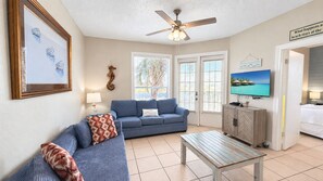 A living room with a blue sofa, a wooden coffee table, and a television on the wall.