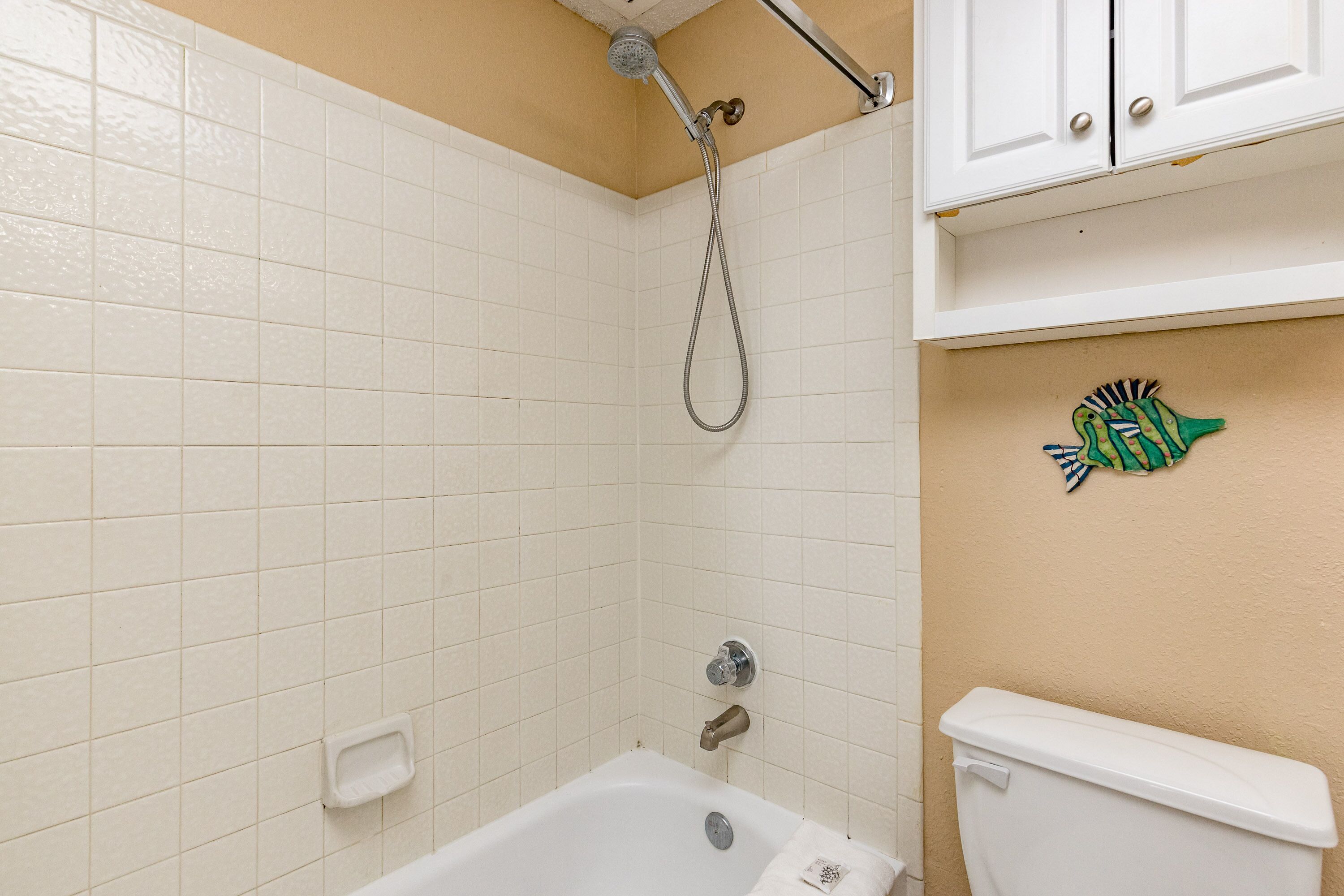 A bathroom with white tiles, a bathtub, a toilet, and a showerhead.