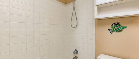 A bathroom with white tiles, a bathtub, a toilet, and a showerhead.