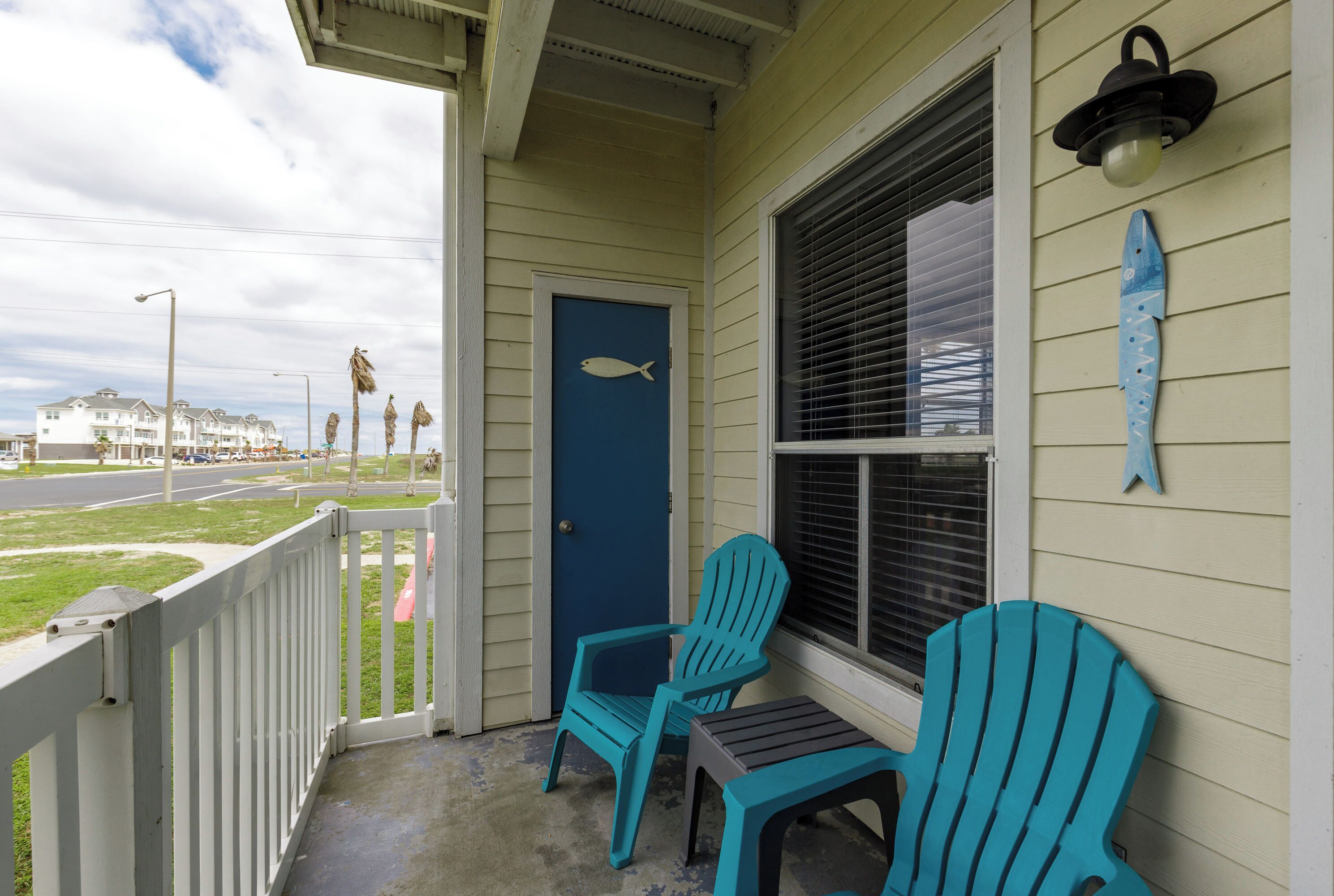 Une véranda avec deux fauteuils Adirondack turquoise et une porte bleue.