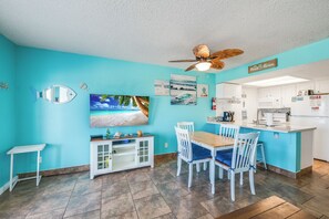 Une cuisine avec un mur bleu, des placards blancs, une table à manger en bois et un ventilateur de plafond.