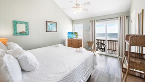A bedroom with a large bed, a dresser, a television, and a balcony with a view of the ocean. - Beachfront Retreat | Pool, Hot Tub & Stunning Ocean Views (Corpus Christi)