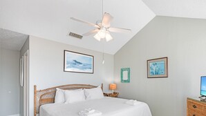 A bedroom with a large bed, a ceiling fan, and two framed pictures on the wall. - Beachfront Retreat | Pool, Hot Tub & Stunning Ocean Views (Corpus Christi)