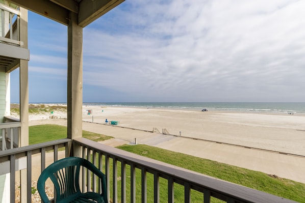 Une vue sur la plage depuis un balcon, avec une chaise, une rambarde en bois et un ciel dégagé.